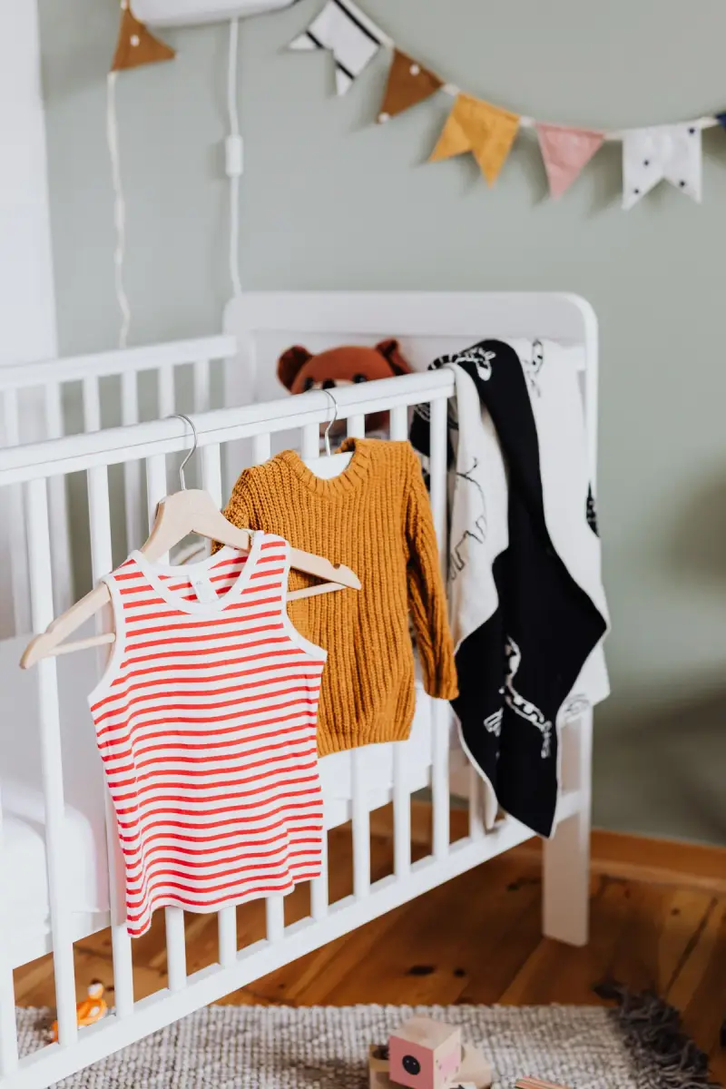 Striped tank, mustard knit and black print top hung on a white crib under bunting