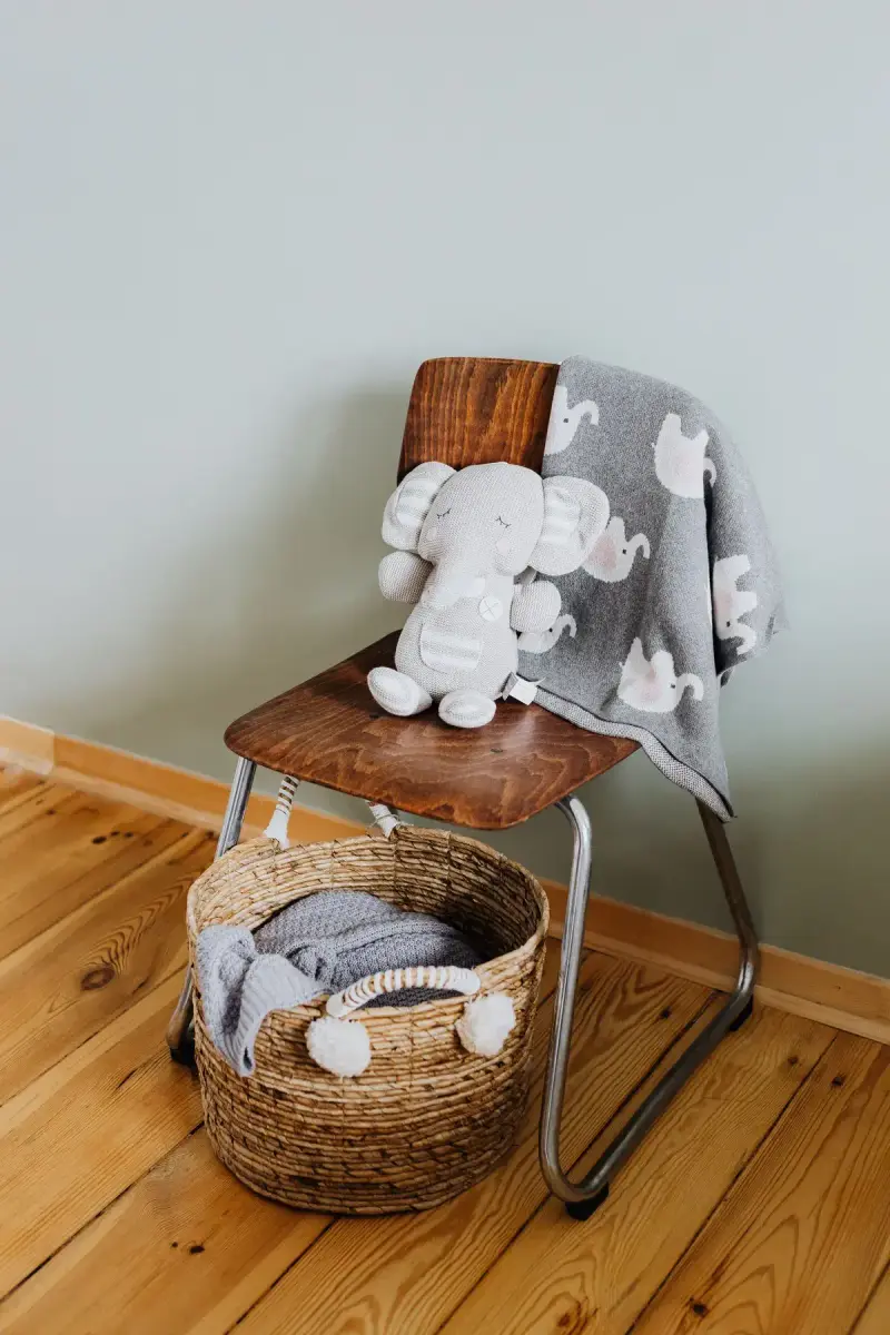 Knit elephant toy and gray baby blanket on a chair above a woven storage basket