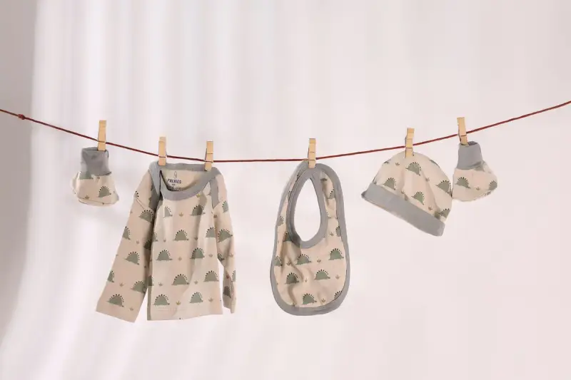 Matching baby top, bib, hat and mittens pegged to a line against a white wall