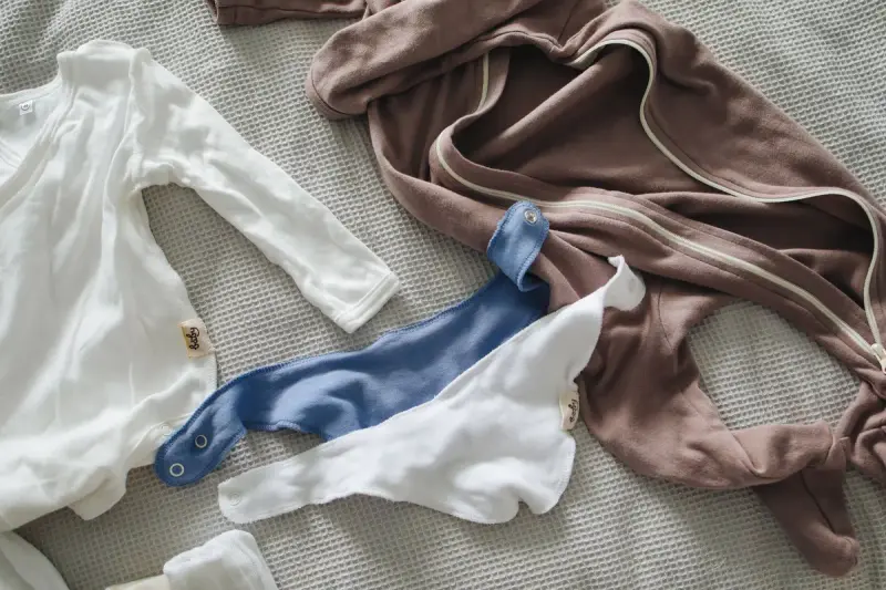 Newborn bodysuits and a sleepsuit laid out on a textured beige bedspread