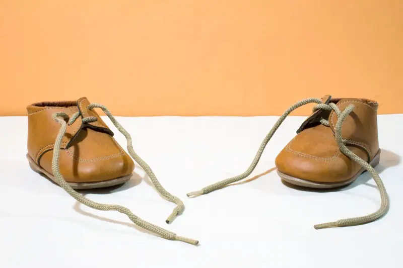 Pair of small brown leather baby shoes with long laces on a white surface