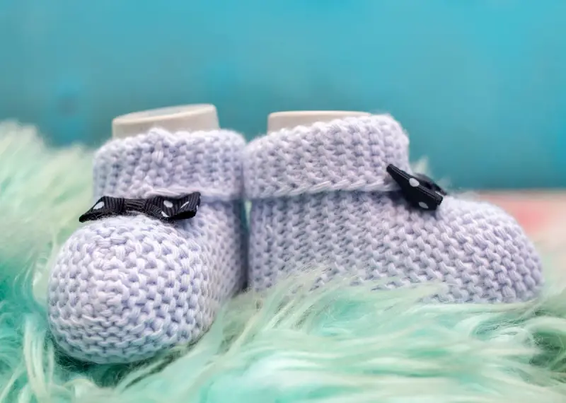 Knitted lilac baby booties with small bows on a fluffy mint rug