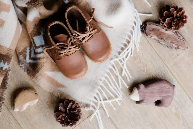 Brown leather children's boots on a plaid blanket with pine cones and wooden toy animals