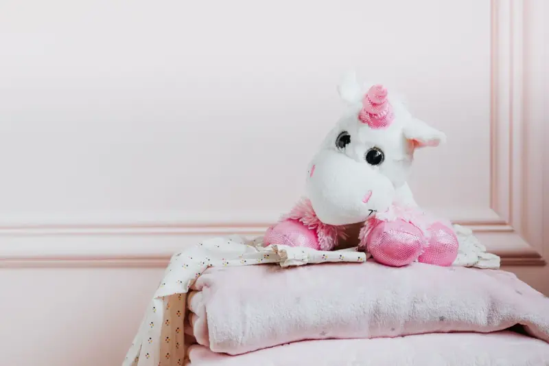 Plush unicorn toy sitting on a stack of folded pink baby blankets