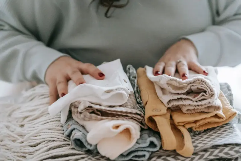 Woman's hands folding stacks of neutral baby clothes on a knit throw