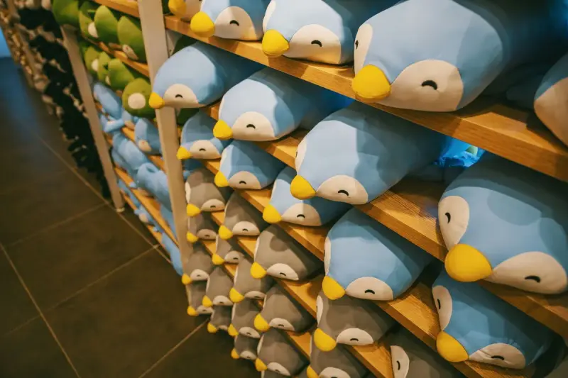 Rows of identical blue and white penguin plush toys stacked on wooden shelves