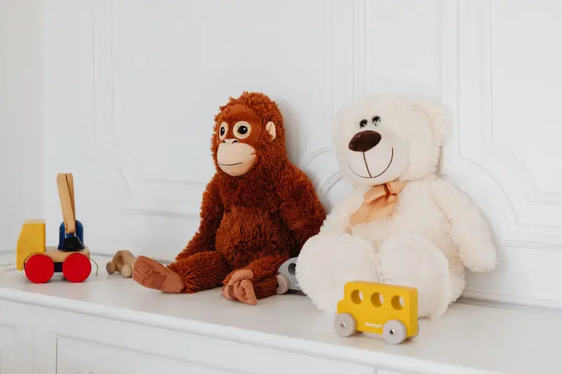 Plush monkey and white teddy bear beside small wooden toy cars on a white shelf
