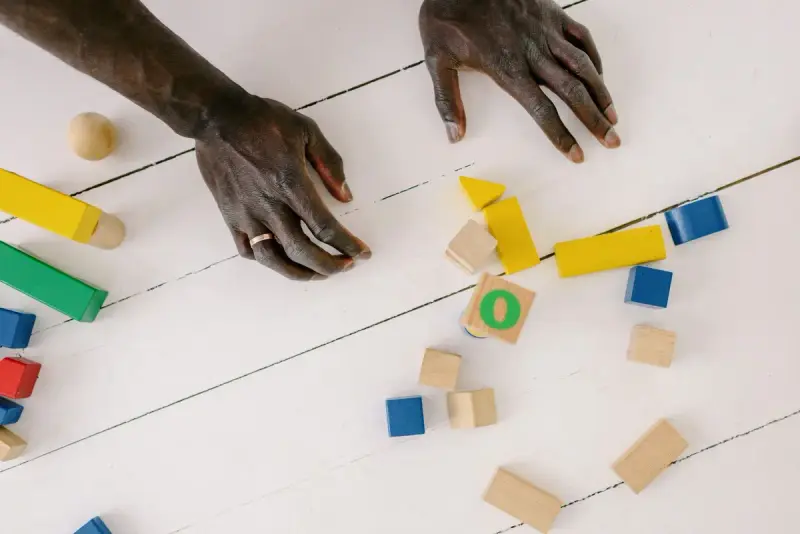 Hands resting on a white wooden table scattered with colorful wooden blocks