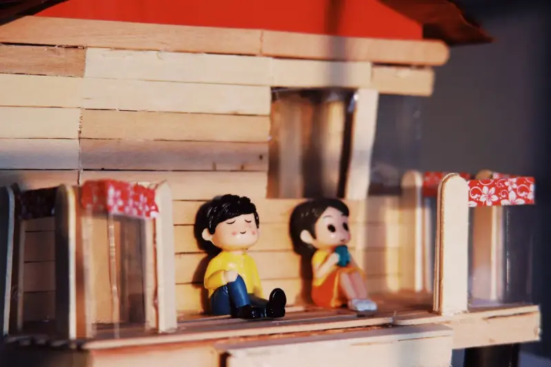 Two small vinyl figurines sitting on the porch of a miniature wooden house