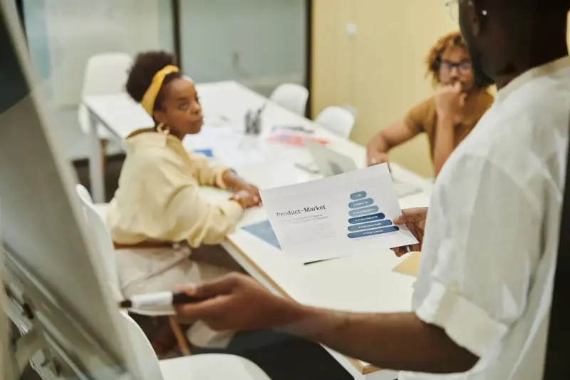 Three colleagues reviewing printed charts together at a white meeting table