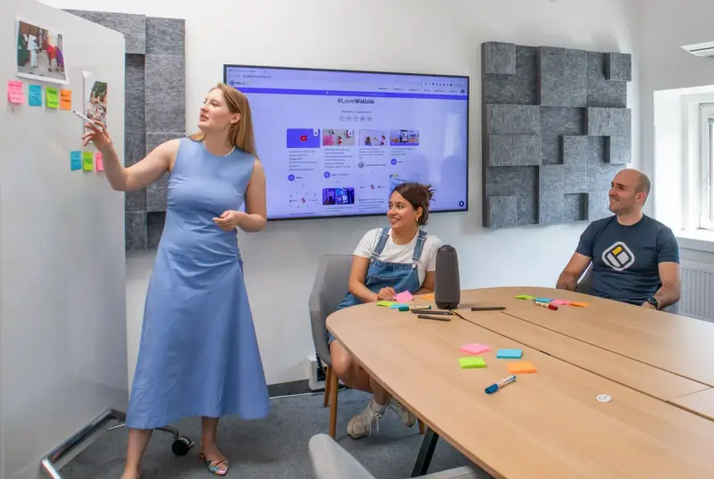 Woman presenting at a wall screen to two colleagues seated at a conference table