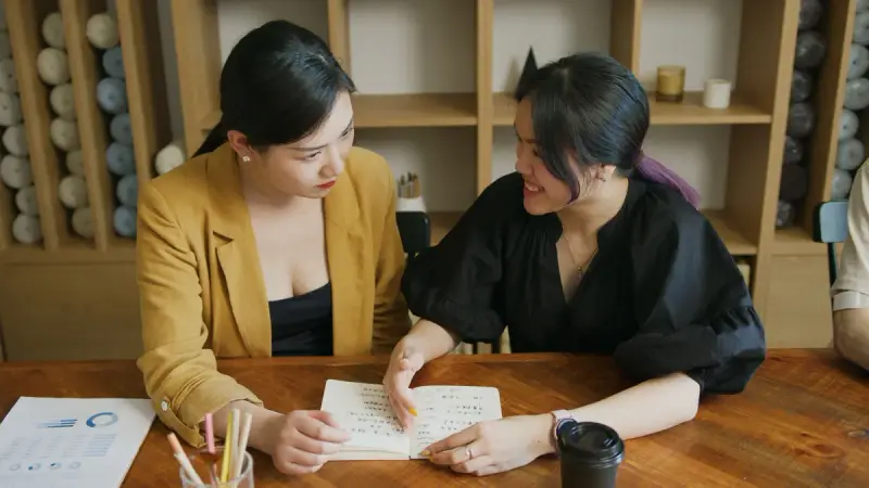 Two women going over notes together at a wooden table in a bright office