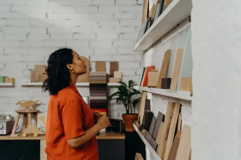 Woman studying samples displayed on wooden shelves along a white brick showroom wall