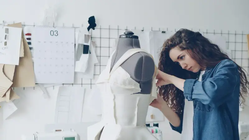 Designer draping white fabric on a dress form in a bright studio
