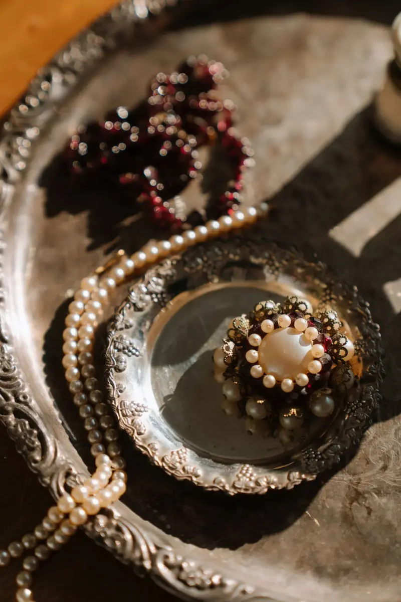 Vintage silver tray holding a pearl and garnet brooch with strands of pearls