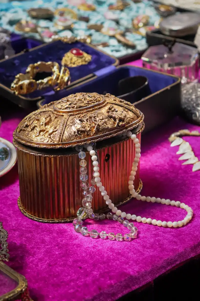 Ornate antique gilt jewelry box with pearl strands on magenta velvet beside vintage rings