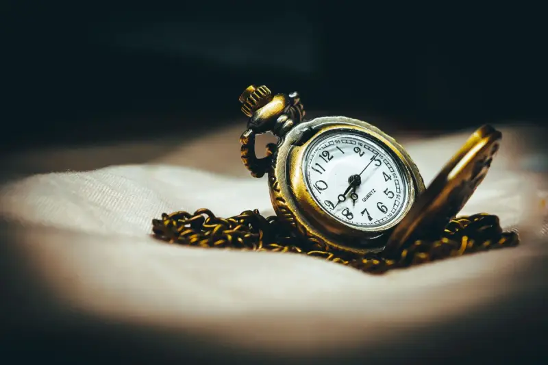 Open brass pocket watch with chain lit by a spotlight on pale fabric