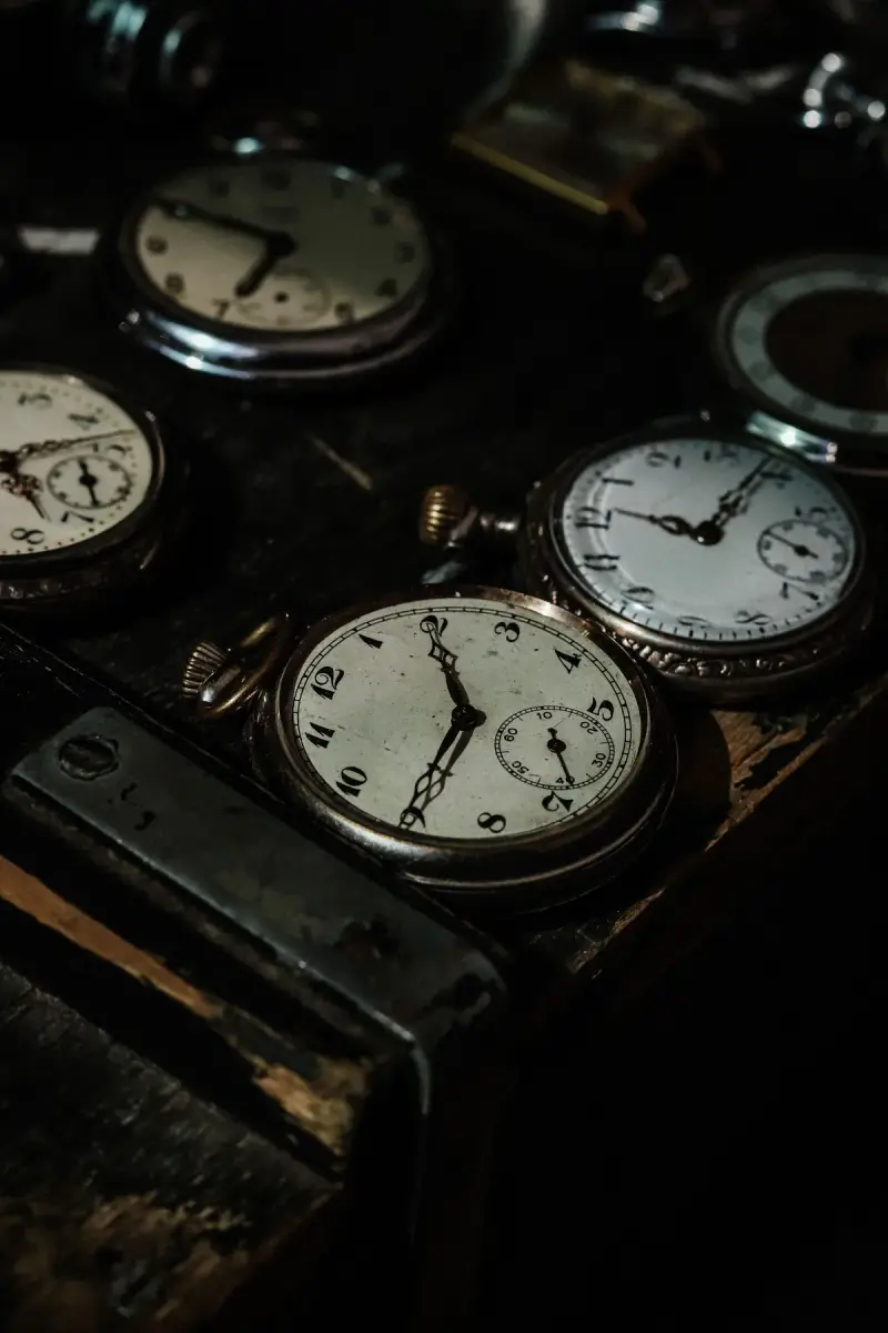 Collection of vintage pocket watches with enamel dials on a dark wooden case