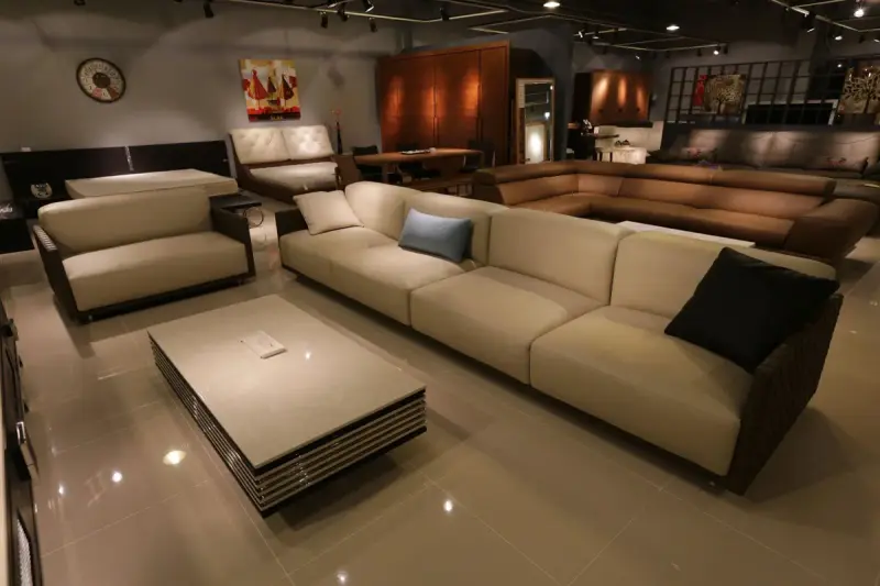 Beige three-seat sofa and lounge chairs around a low coffee table in a warmly lit furniture showroom