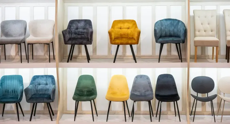 Two rows of upholstered dining chairs in gray, mustard, teal and green on white display shelves
