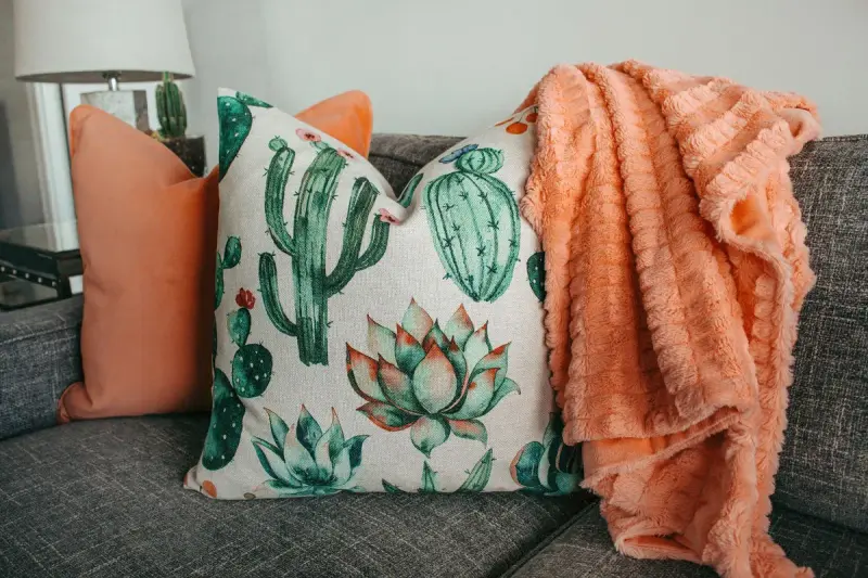 Cactus-print throw pillow, coral cushion and textured coral blanket on a gray sofa