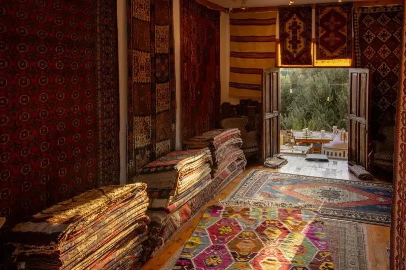 Warmly lit room stacked and hung with red and multicolor handwoven rugs