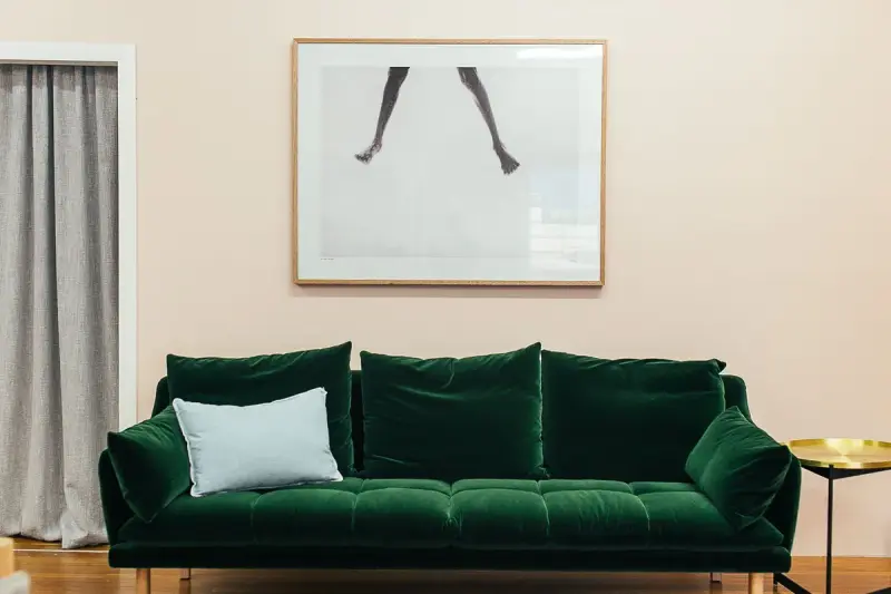 Green velvet sofa with a pale cushion beneath framed art in a bright minimalist room