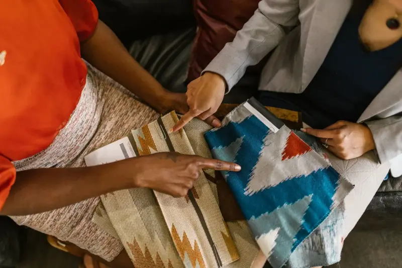 Two people pointing at patterned upholstery fabric swatches spread across a sofa