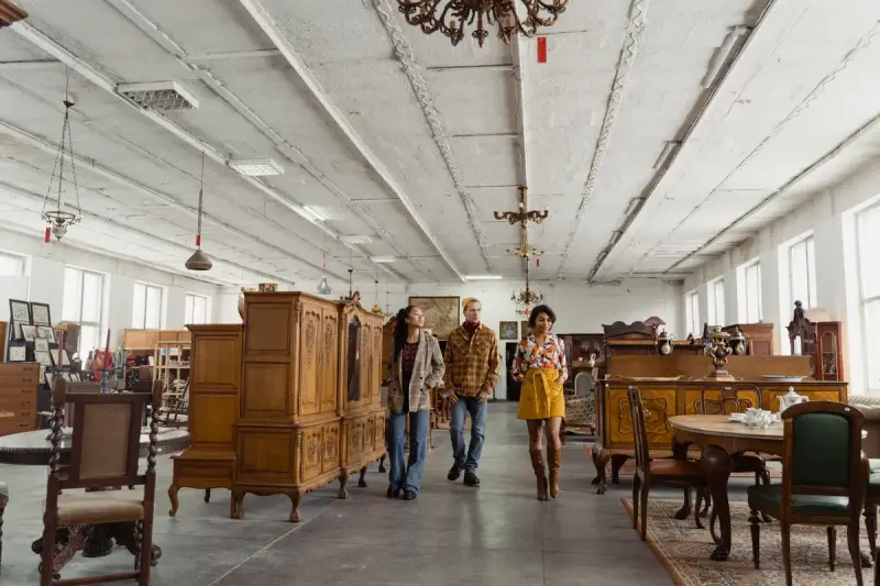 Three shoppers walking through a large hall lined with wooden cabinets and dining sets