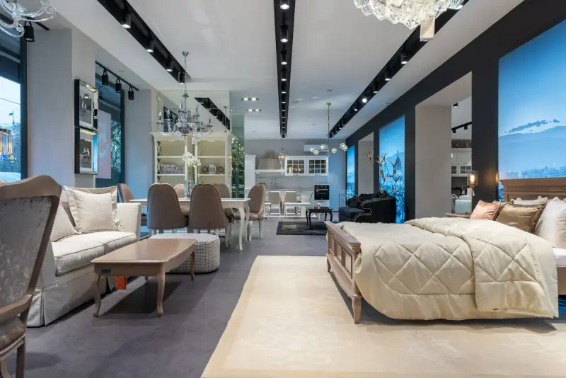 Long furniture store floor with a made bed, sofas, dining tables and cabinets under rows of lights