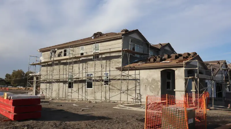 Two-story wood-frame house under construction with scaffolding and a tiled roof