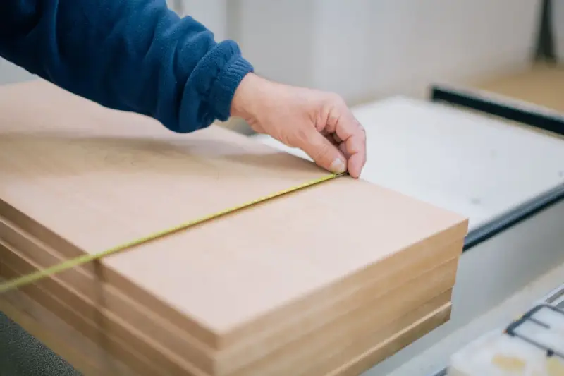 Hand stretching a tape measure across stacked wooden planks