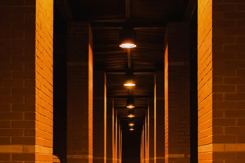 Brick corridor with a row of pillars lit by warm ceiling lights receding into the distance