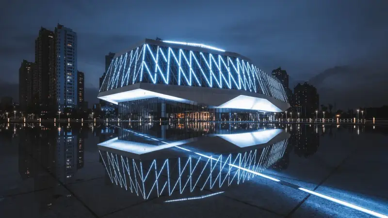 Glass building lit with LED lines at night, its light reflected in still water