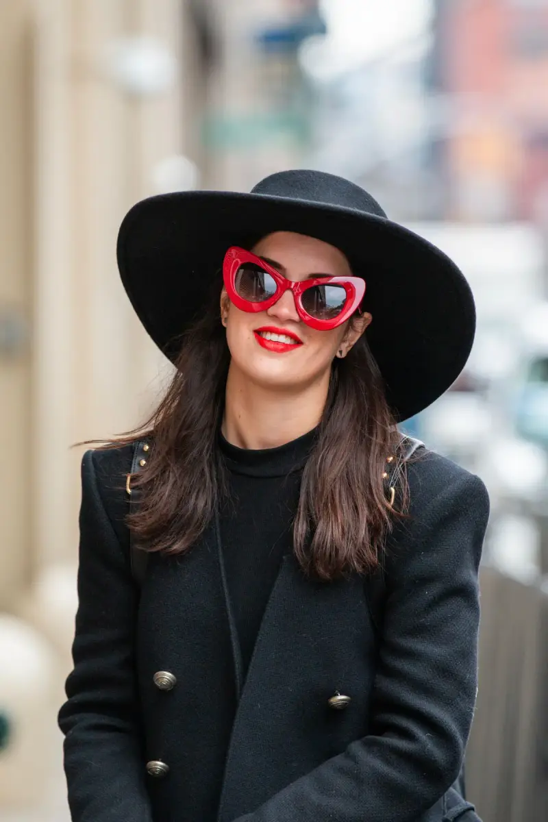 Woman in red cat-eye sunglasses and a wide black hat on a New York street