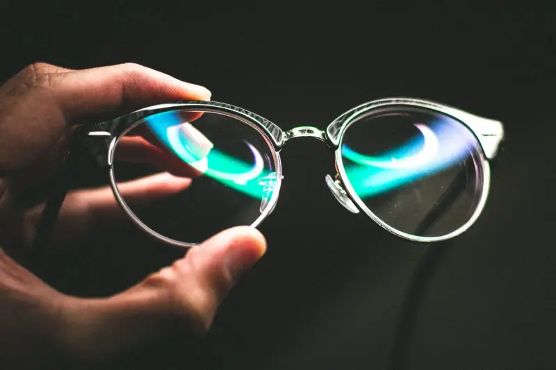 Hand holding reflective eyeglasses against a black background