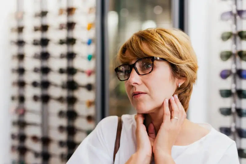 Woman trying on dark eyeglass frames in front of a frame display