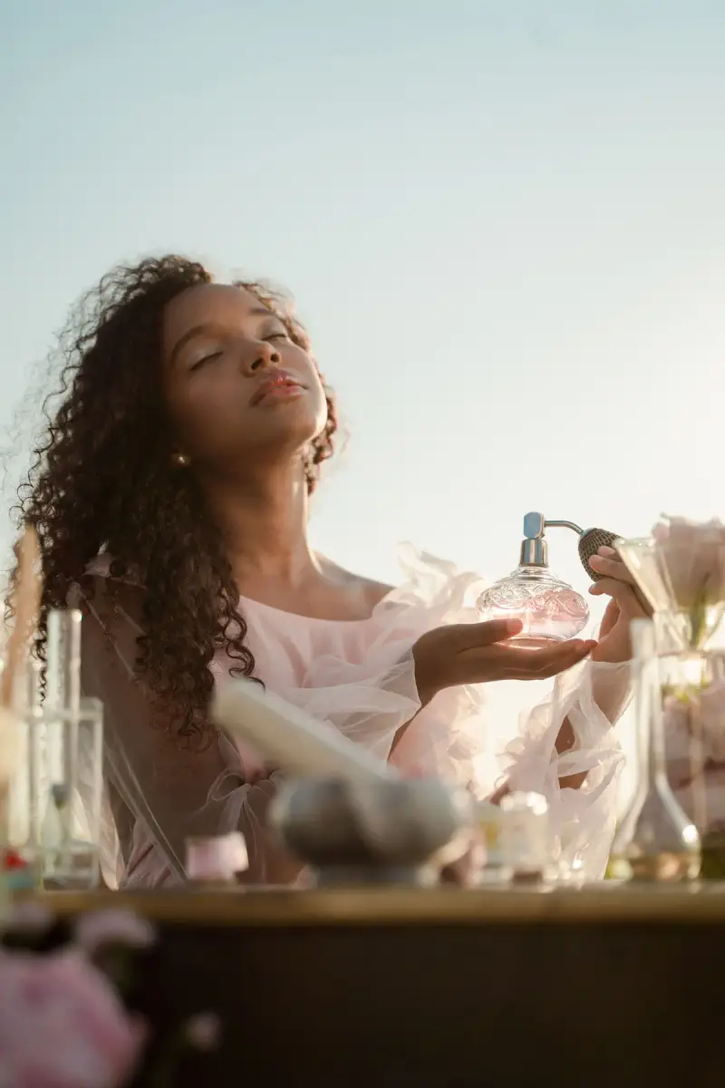 Woman with curly hair spraying perfume from a vintage glass atomizer