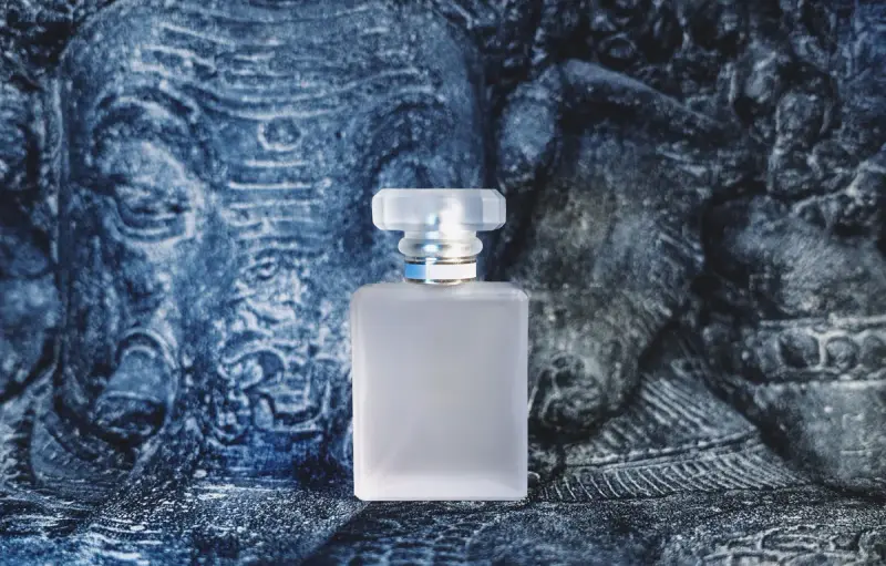 Frosted glass perfume bottle with clear cap on a carved blue backdrop