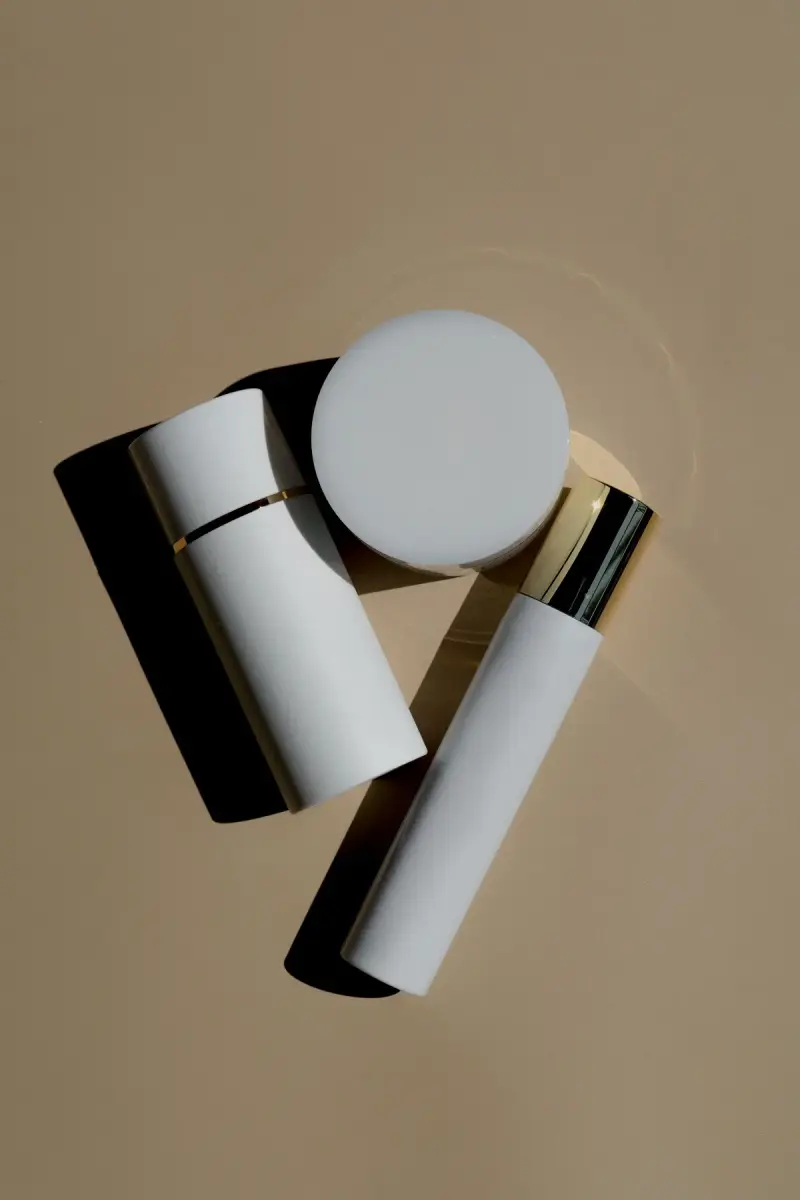 White cosmetic tubes and a jar with a gold collar on a beige background