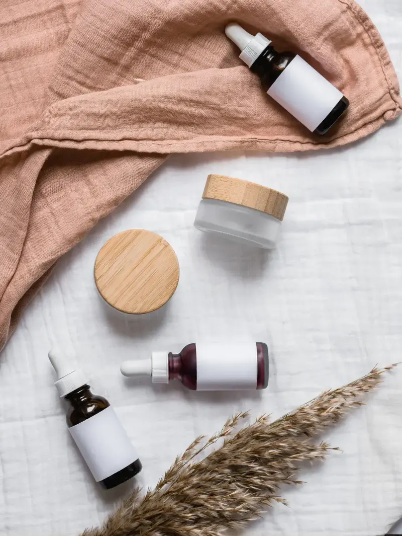 Amber dropper bottles and bamboo lid jars on linen with dried grass