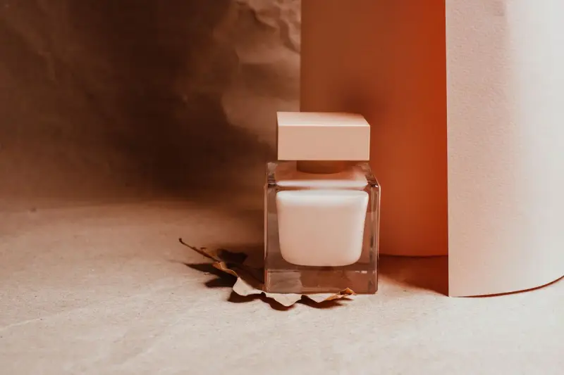 Square glass cream jar with a blush lid on a sculpted paper backdrop