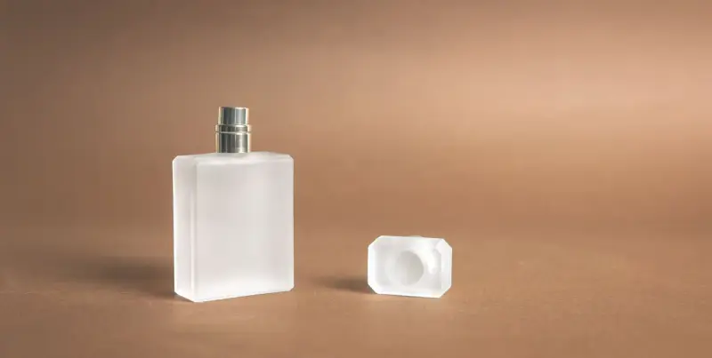 Frosted square perfume bottle with its cap set beside it on a warm brown backdrop