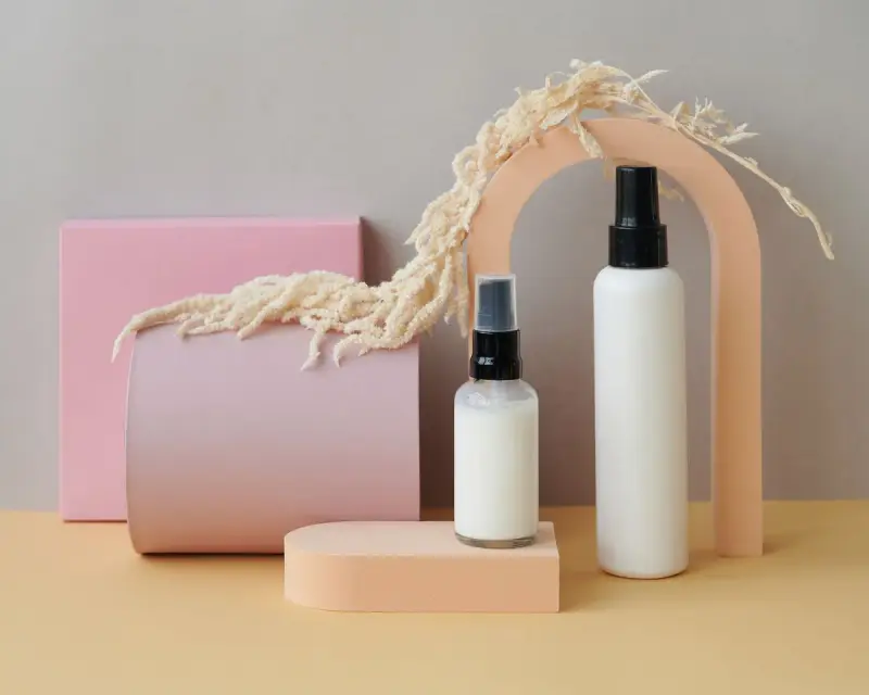 Unbranded white bottles and pump dispensers arranged with pastel shapes and dried grass