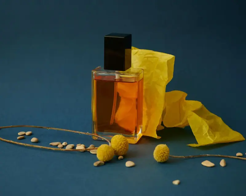 Amber perfume bottle with a black cap beside yellow paper on a teal background