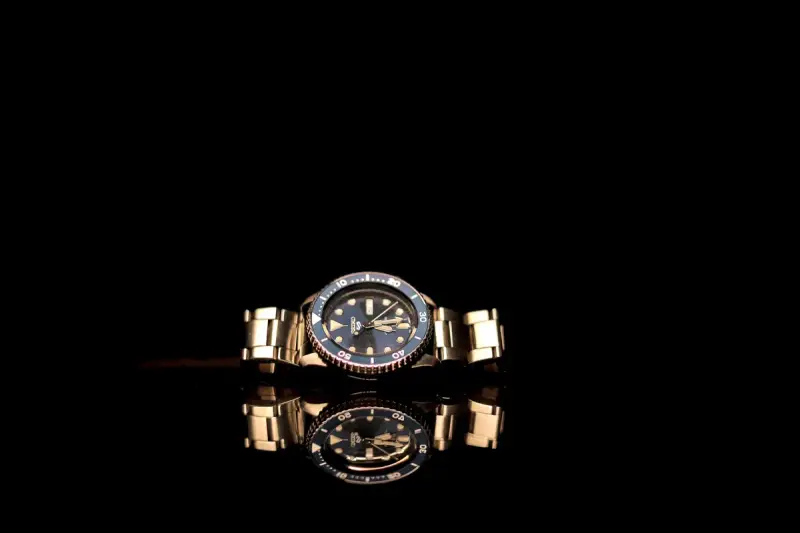 Gold wristwatch with a black dial reflected on a glossy surface