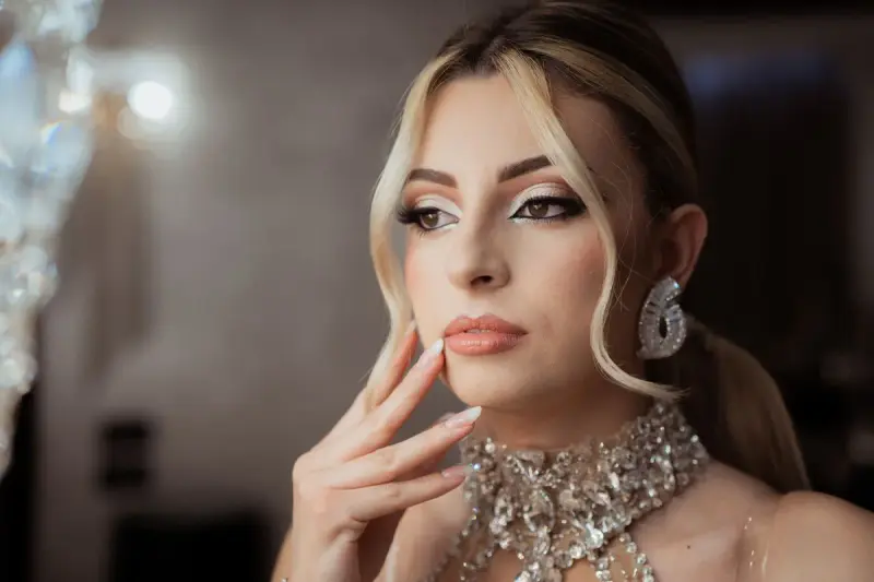 Woman in evening makeup touching her face, wearing a crystal collar necklace and drop earrings