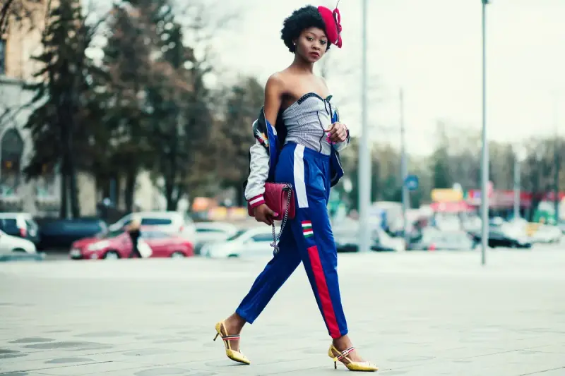 Woman in blue track pants with a red stripe and heels crossing a city street