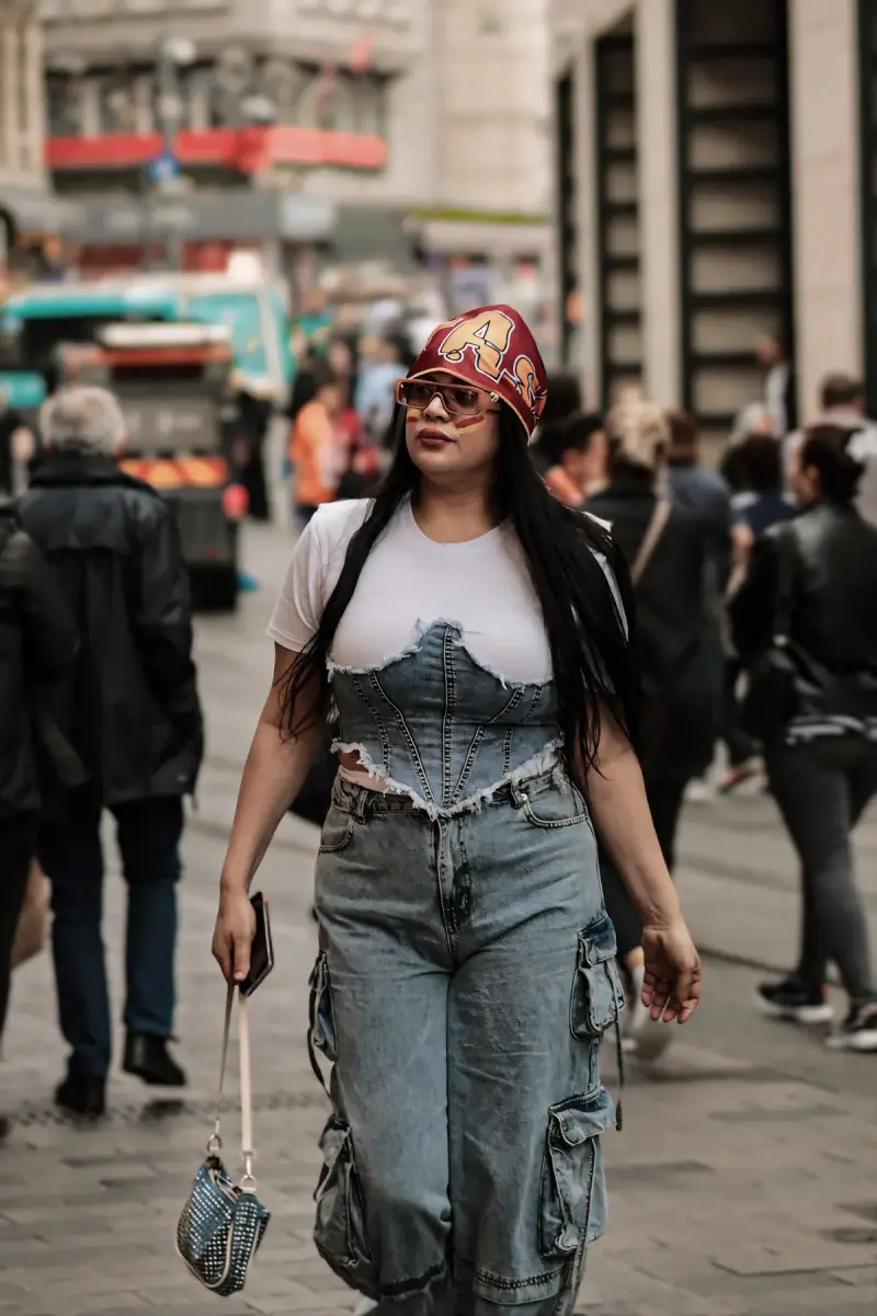 Young woman in a denim corset top, cargo jeans and headscarf walking a busy street