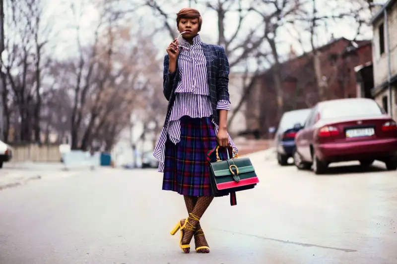 Woman in a plaid skirt, lilac shirt and denim jacket with a striped handbag on a city street